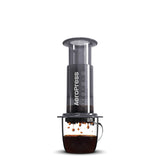 Aeropress coffee brewing kit, (plastic) including aeropress chamber, plunger, filter holder, filter cap, stir stick, scoop, and funnel. pictured on a white background.