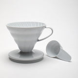 hario v60 (02) white plastic dripper with a small plastic measuring cup. pictured on a white background.