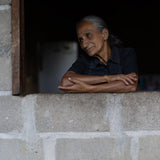 Old woman leaning on a stone wall with a dark interior background