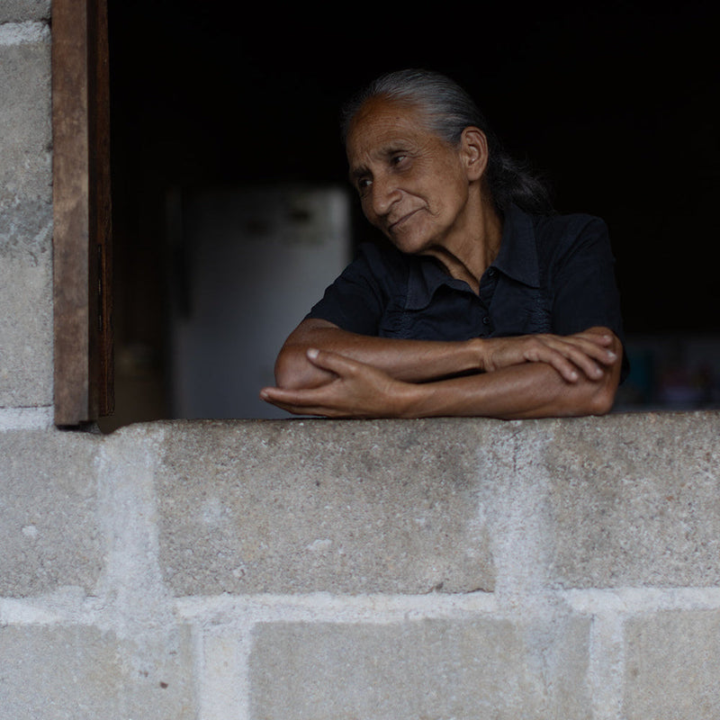 Old woman leaning on a stone wall with a dark interior background