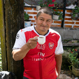coffee farmer wearing arsenal soccer jersey sipping on a cup of coffee outside